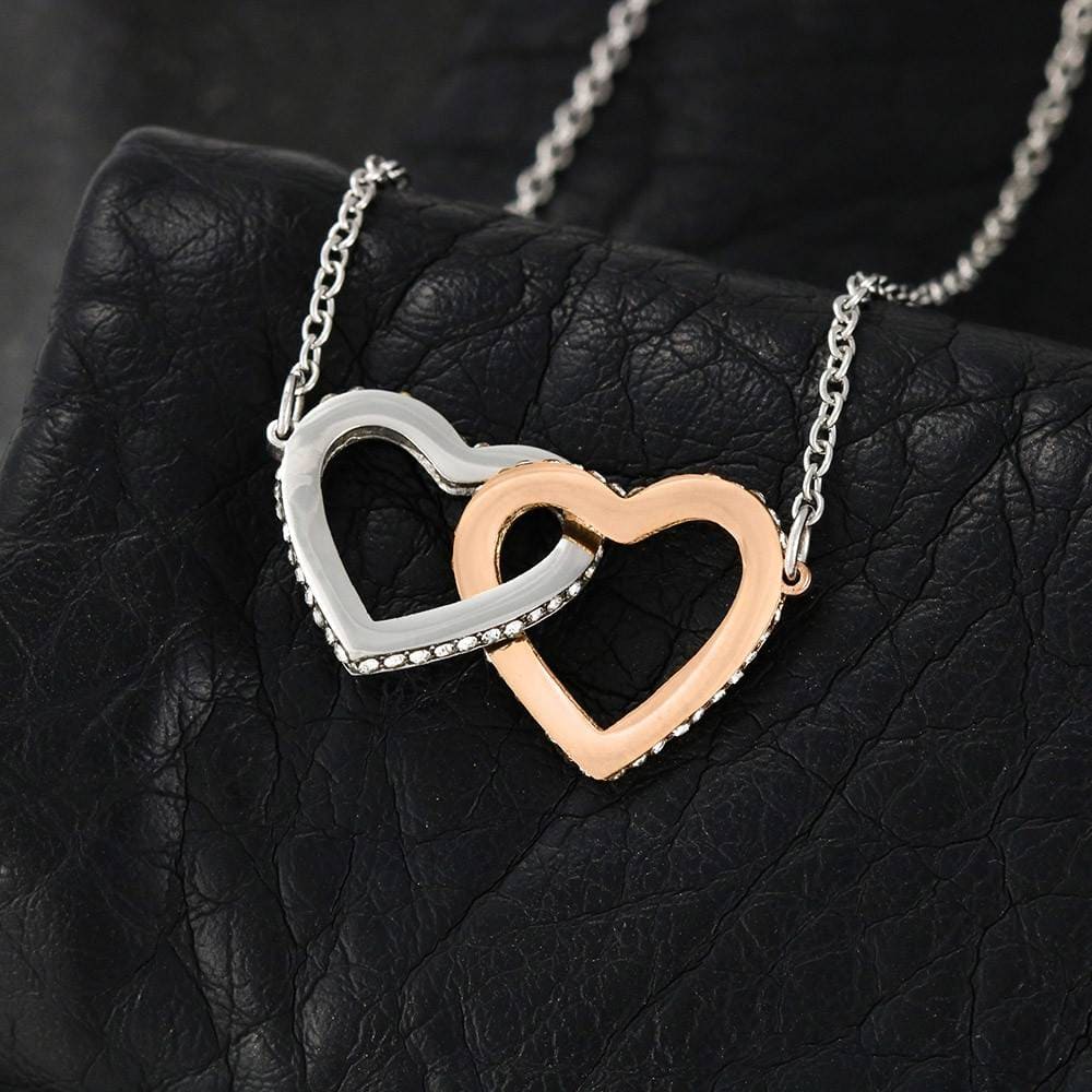 Interlocking Hearts Necklace with cubic zirconia crystals, lying open in a mahogany gift box with LED spotlight reflecting off the hearts